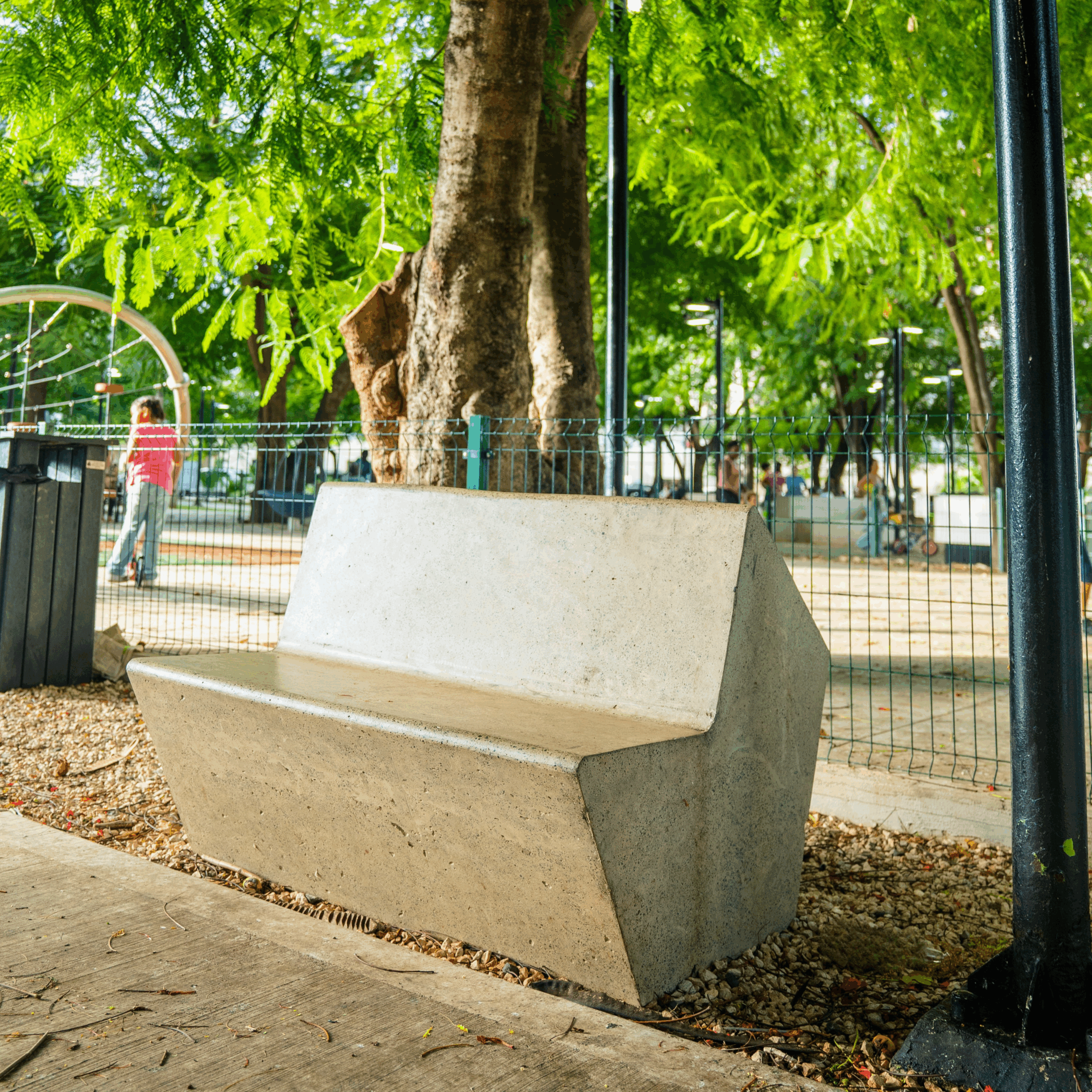 "Banco de concreto reforzado en parque urbano con juegos infantiles y espacios comunes frente a clínica y residenciales"